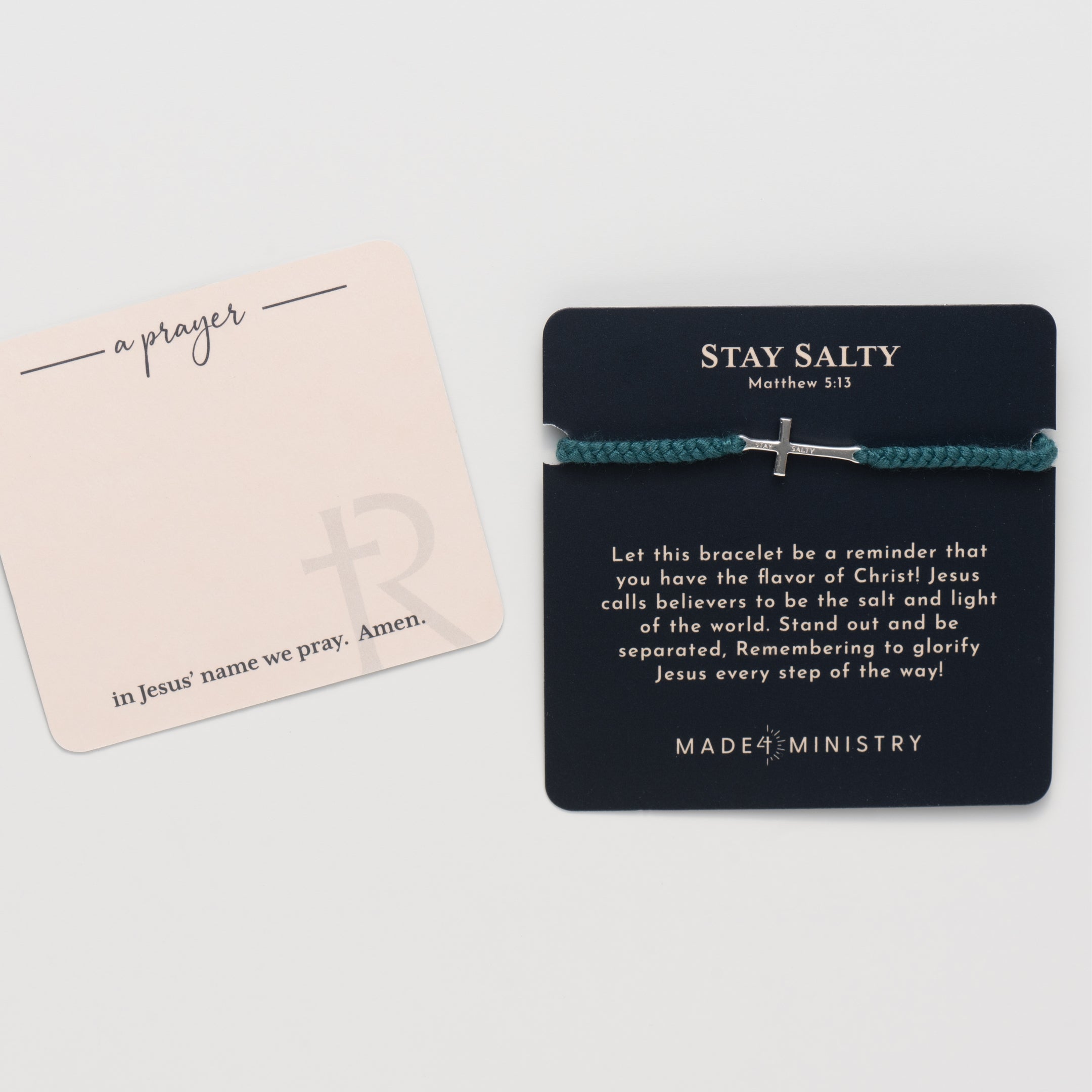 Cross bracelet engraved STAY SALTY set on a naturally dyed azure blue hand-braided, cotton cord friendship bracelet with a  Sterling Silver finish from the Made4Ministry Collection by Rizen Jewelry. Featured on a devotion card laying next to the prayer card. 