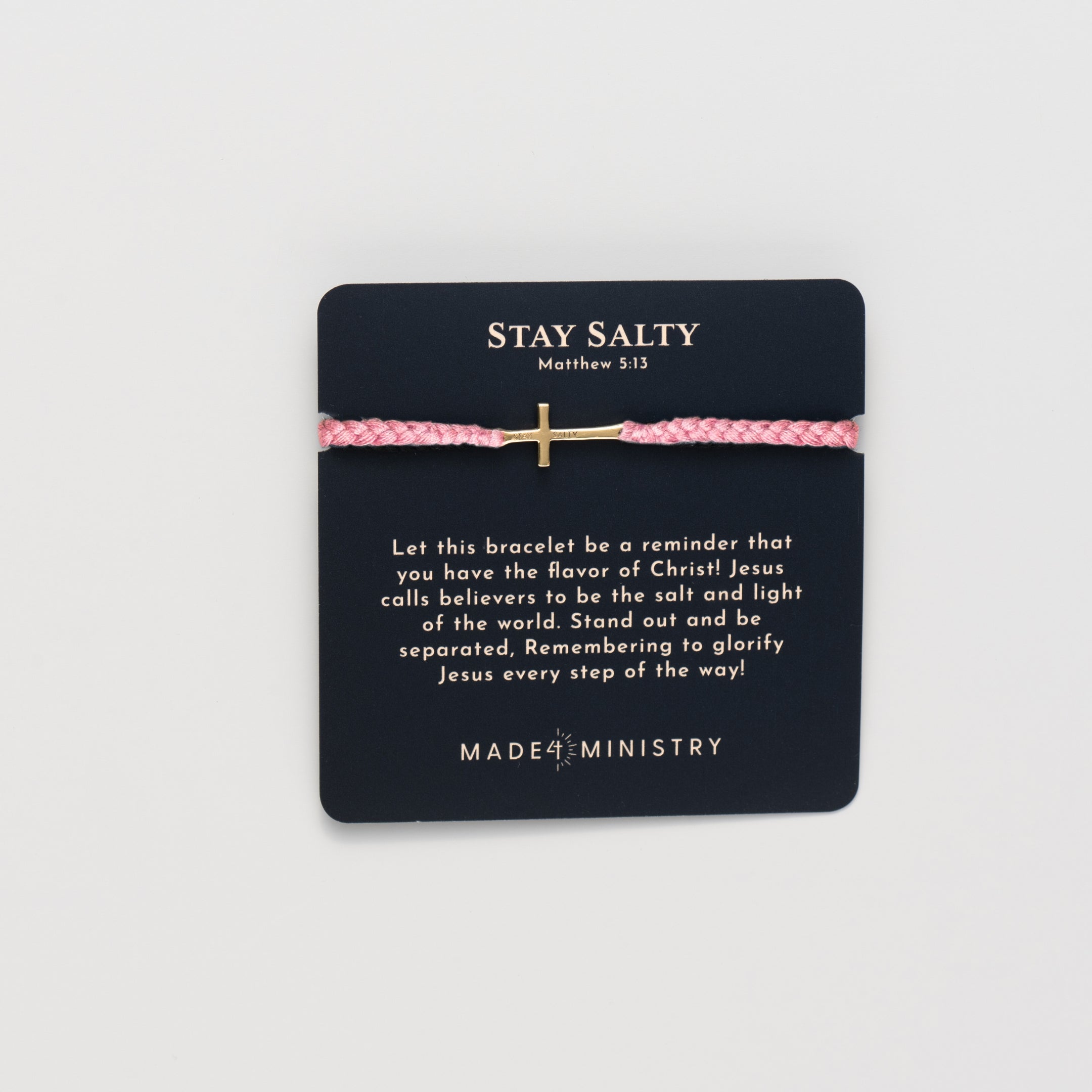 Cross bracelet engraved STAY SALTY set on a naturally dyed dusty rose hand-braided, cotton cord friendship bracelet with a gold or sterling silver finish from the Made4Ministry Collection by Rizen Jewelry. Featured on a devotion card. 