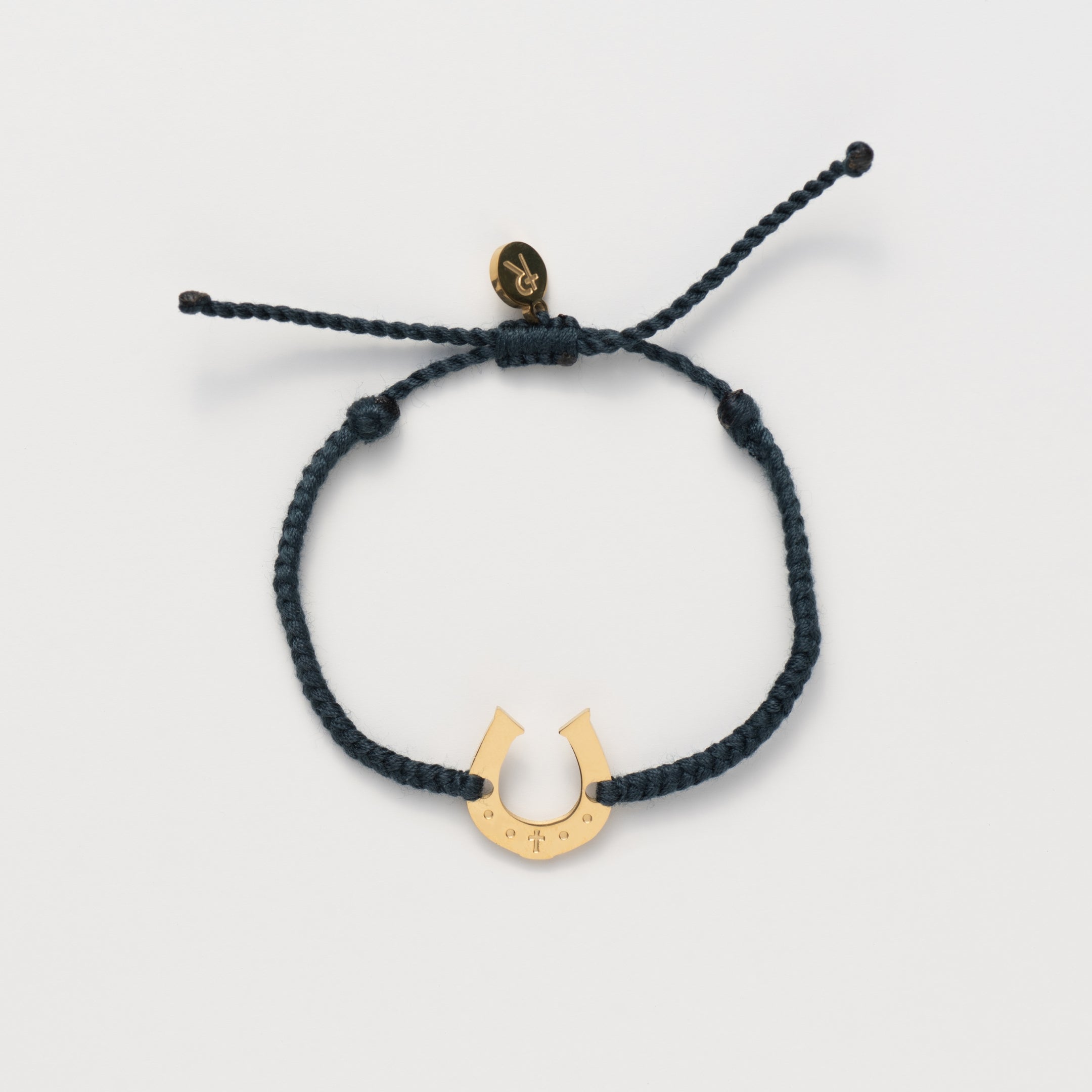 Horseshoe bracelet engraved with a cross set on a naturally dyed black hand-braided, cotton cord friendship bracelet. Available in 18k Gold and Sterling Silver finish.