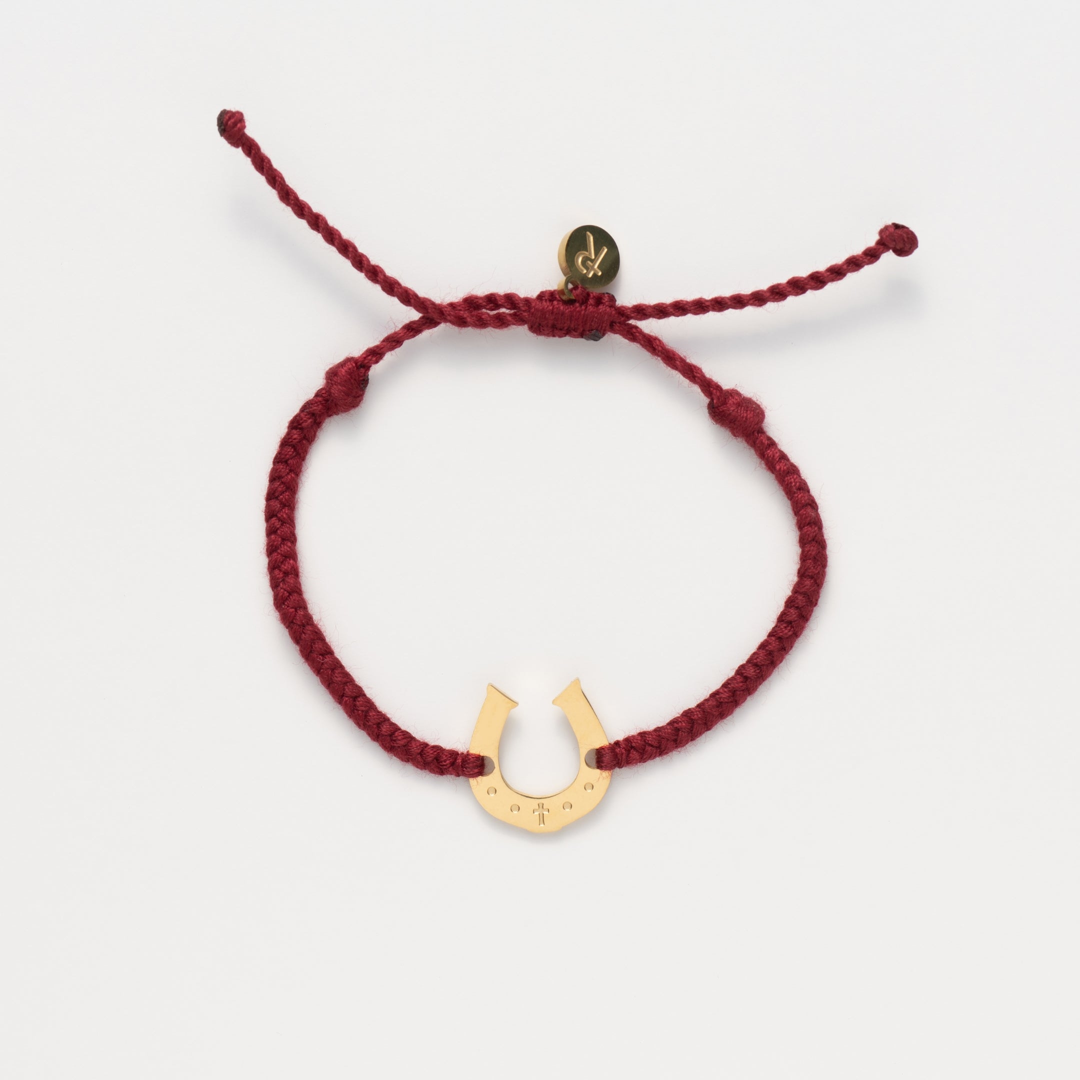 Horseshoe bracelet engraved with a cross set on a naturally dyed garnet red hand-braided, cotton cord friendship bracelet. Available in 18k Gold and Sterling Silver finish. Designed by Rizen Jewelry for the Made4Ministry Collection. 