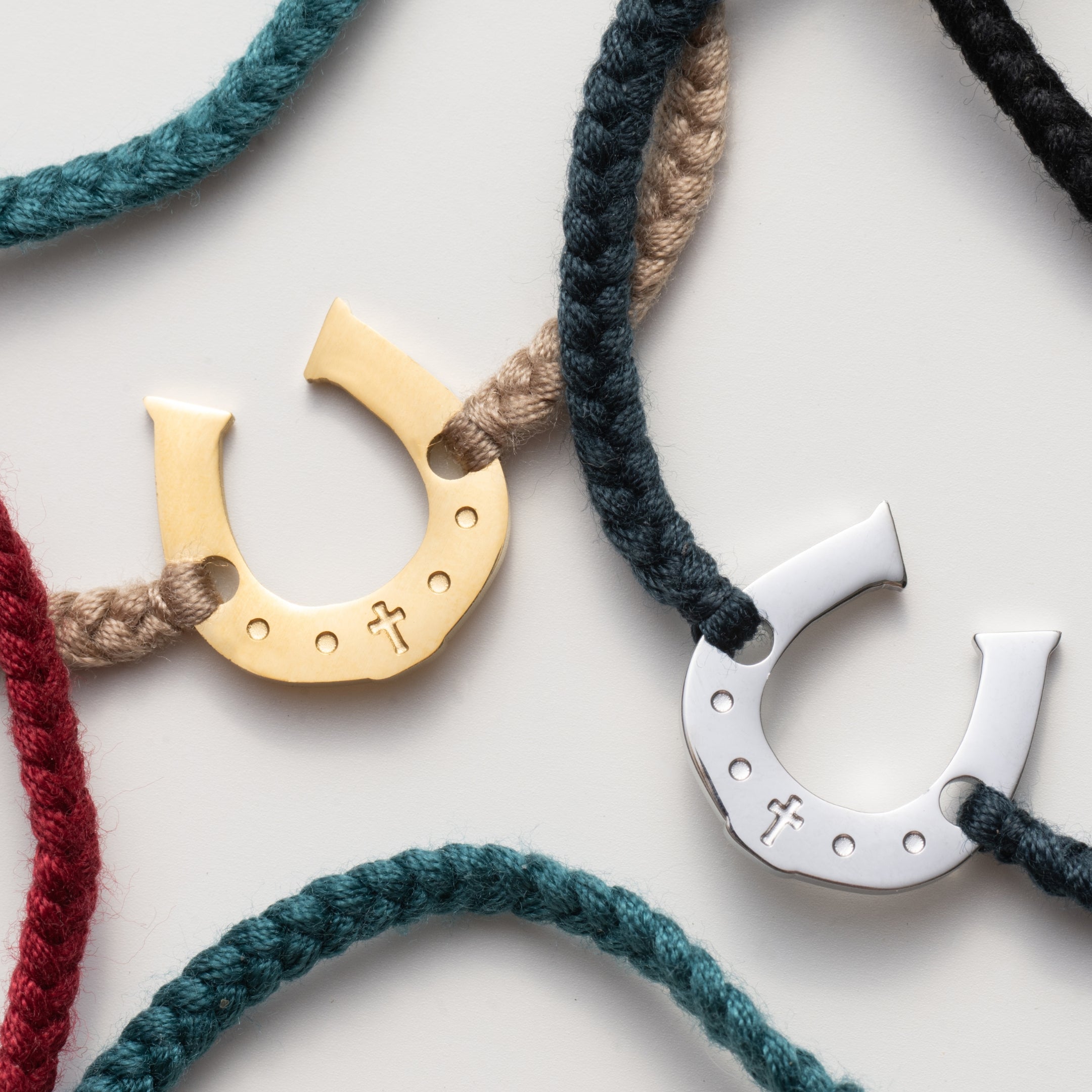 Close Up of the Horseshoe bracelet engraved with a cross set on a naturally dyed cotton cord friendship bracelets. Available in 18k Gold and Sterling Silver finish. Designed by Rizen Jewelry for the Made4Ministry Collection. 