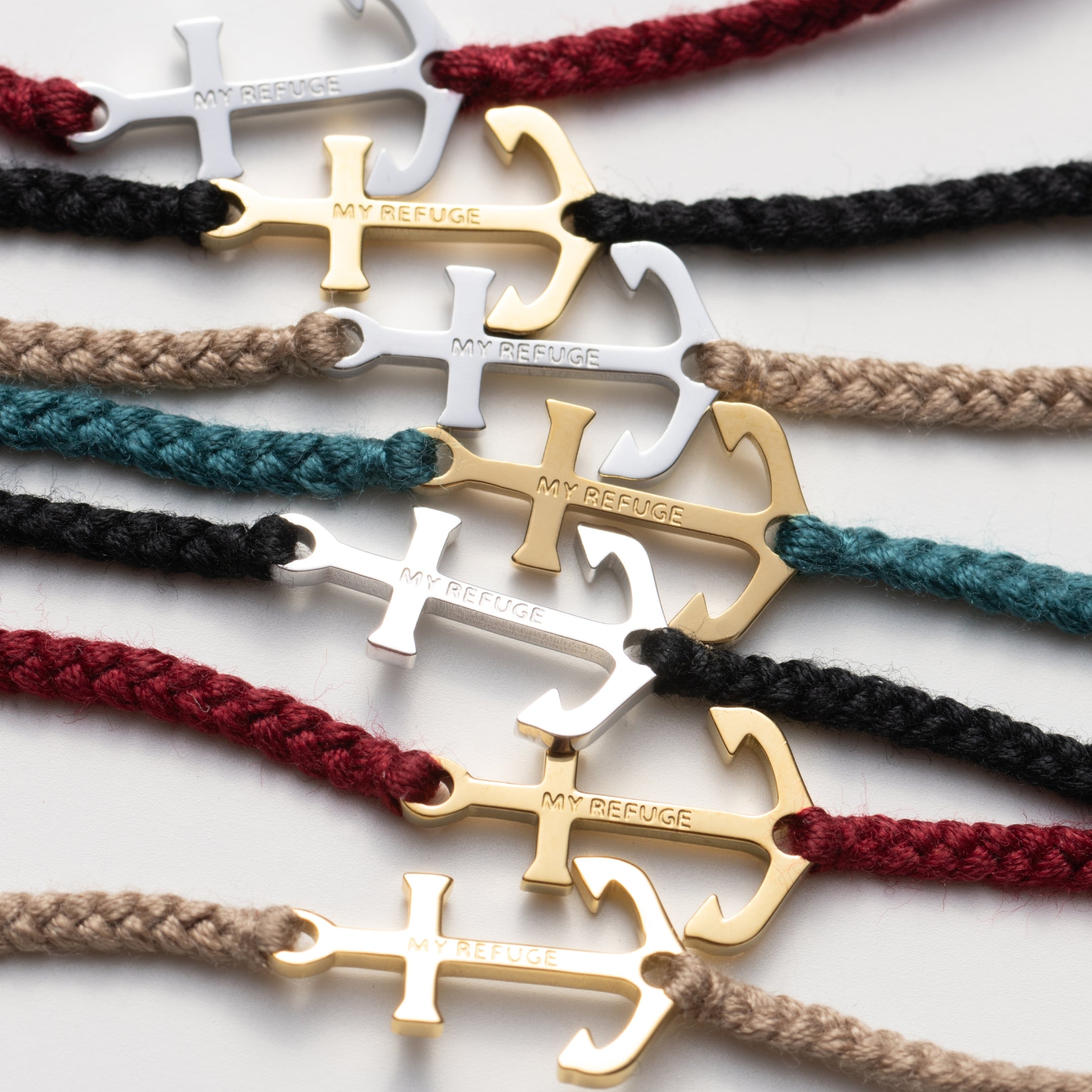 Anchor bracelets with 'My Refuge' engraved on various braided color cord bracelets on a light background from the MAde4Ministry Collection by Rizen Jewelry. 