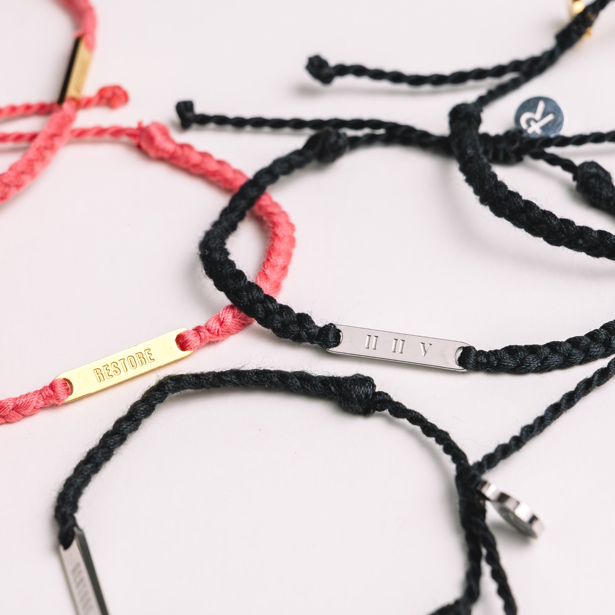 Restore Made4Ministry black and  pink dusty rose cord bracelets x Britt Nicole from her new album IIV featuring the verse Joel 2:25. The gold bar pendant is engraved RESTORE on the front and IIV on the back. 