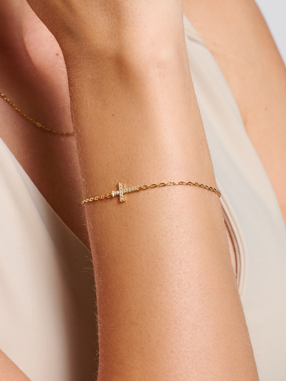 Female model wearing the Delicate Cross Chain Breaker Bracelet, an 18k gold-plated pavé cross bracelet resting on her wrist by Rizen Jewelry