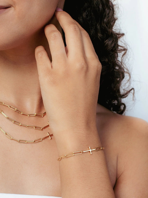 Women's Christian jewelry model is wearing the Chain breaker cross bracelet in 18k gold plated alongside three necklaces from the Calvary collection.  A timeless baptism gift by Rizen Jewelry.