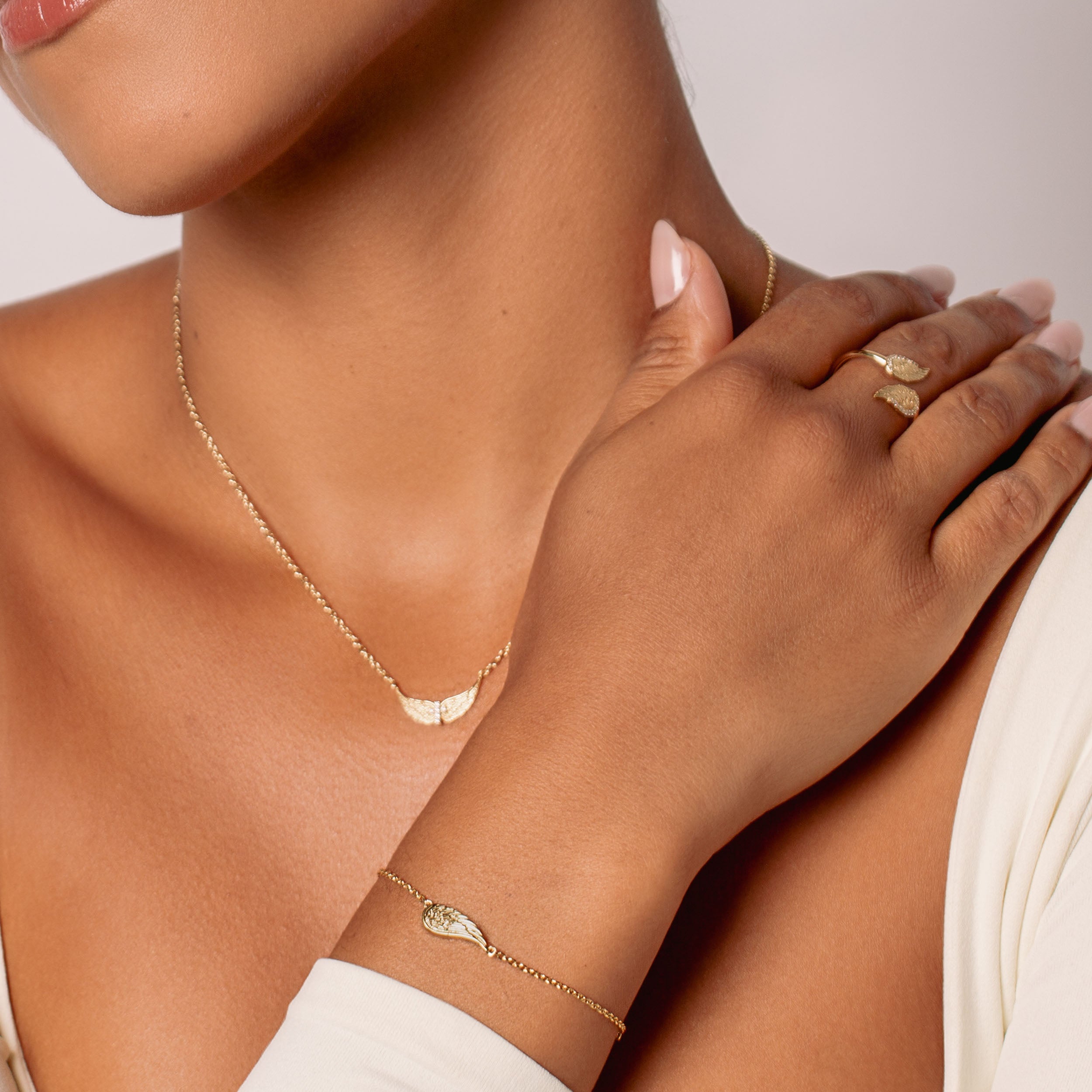 Women's christian jewelry model wearing the divine angel wings bracelet, ring and necklace in 18k plated gold over sterling silver by Rizen Jewelry. 