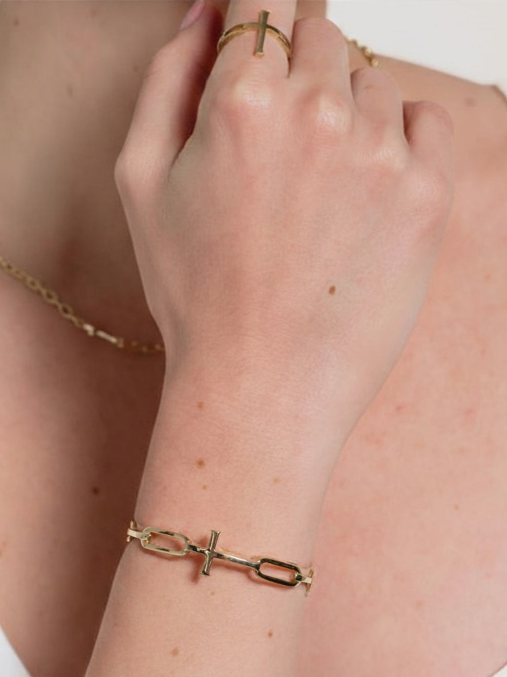 Woman Christian jewelry model wearing the silver bold yet sleek cross cuff bangle featuring striking links seamlessly transitioning into the classic Rizen Cross in heavy 18k gold plating. 