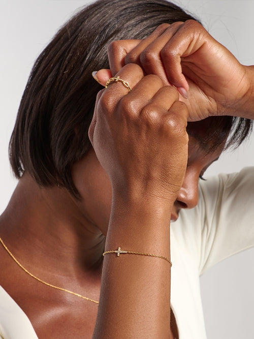 Female model wearing the Dainty Luminous Cross Pavé Bracelet on her wrist, an elegant faith-inspired gold accessory.