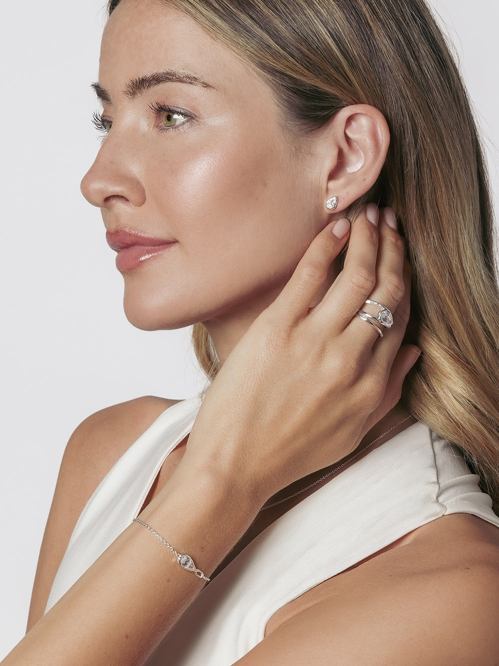 A close-up lifestyle shot of a christian woman wearing the Rizen Jewelry Solace Teardrop Collection which features a necklace, bracelet, ring and earrings. A delicate silver bracelet with a teardrop pendant and a matching silver ring and earring.