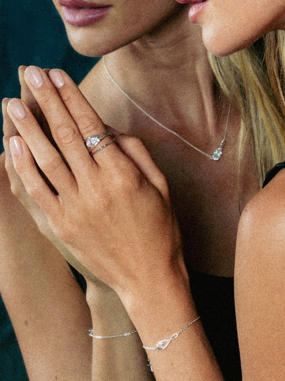 A close-up lifestyle shot of a christian woman wearing the Rizen Jewelry Solace Teardrop Collection which features a necklace, bracelet, ring and earrings. A delicate silver bracelet with a teardrop pendant and a matching silver ring and earring.