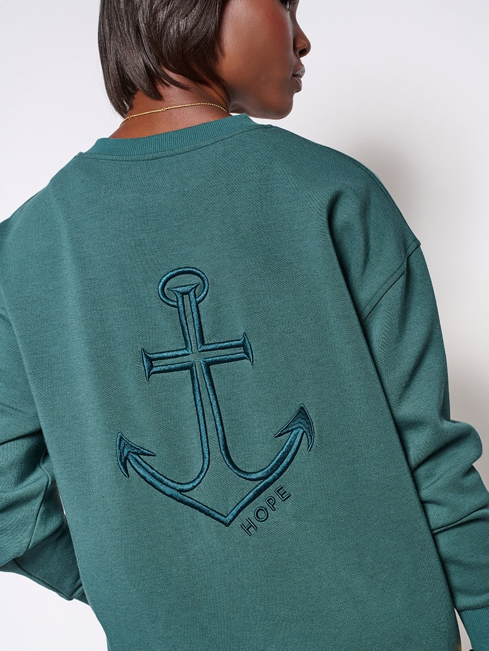 Christian female sweatshirt model wearing dark teal Hope anchor sweatshirt styled with leggings