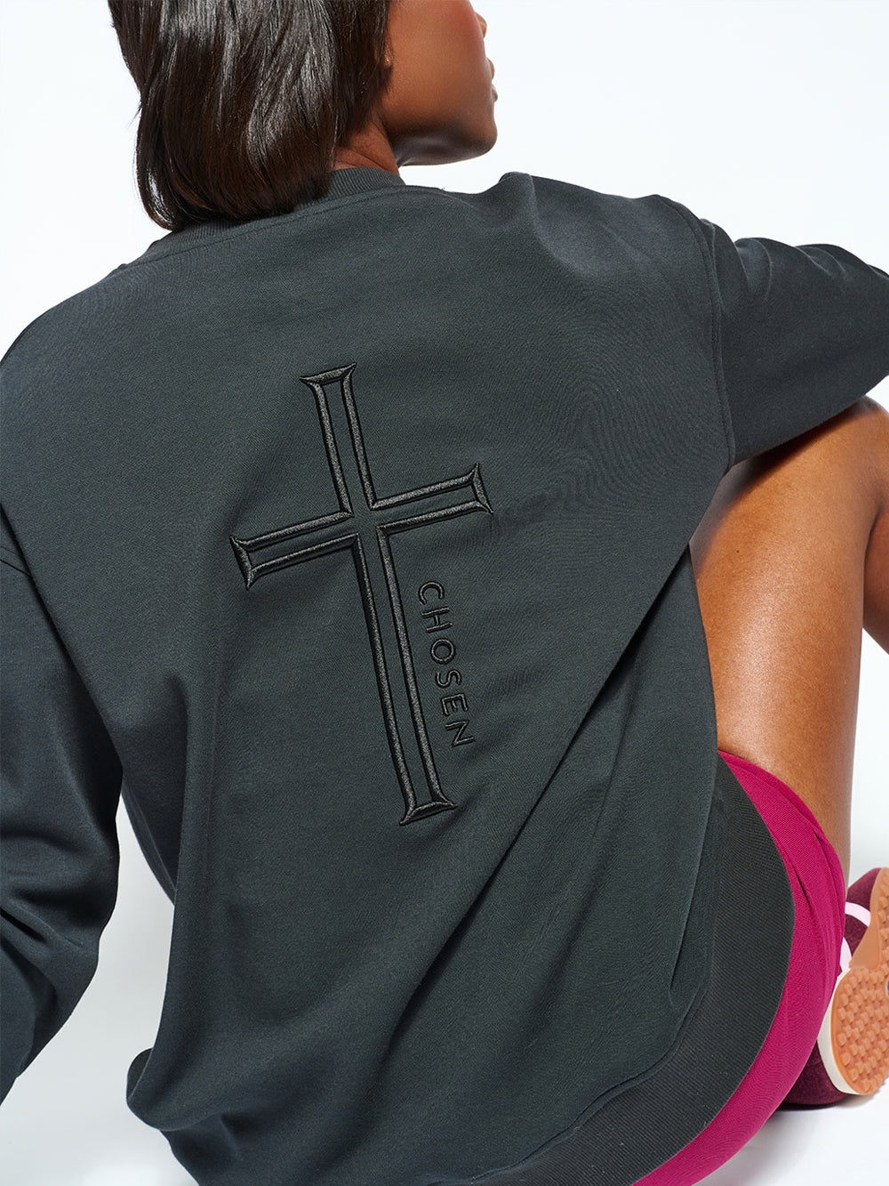 Female christian sweatshirt model contemplating the back of her Chosen sweatshirt featuring cross embroidery with CHOSEN sentiment
