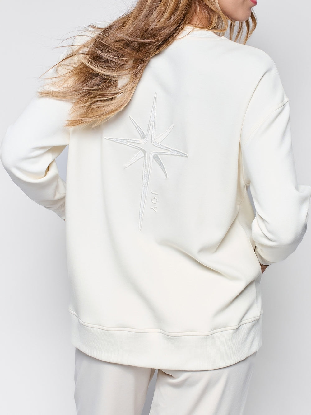 Christian woman's sweatshirt model wearing Joy crewneck sweatshirt with a large embroidered star styled with lounge wear.