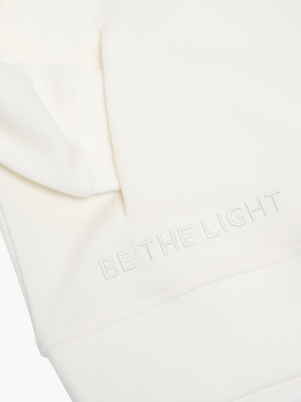 Close-up of Be The Light embroidery and discreet front pockets on premium relaxed-fit crew neck sweatshirt.