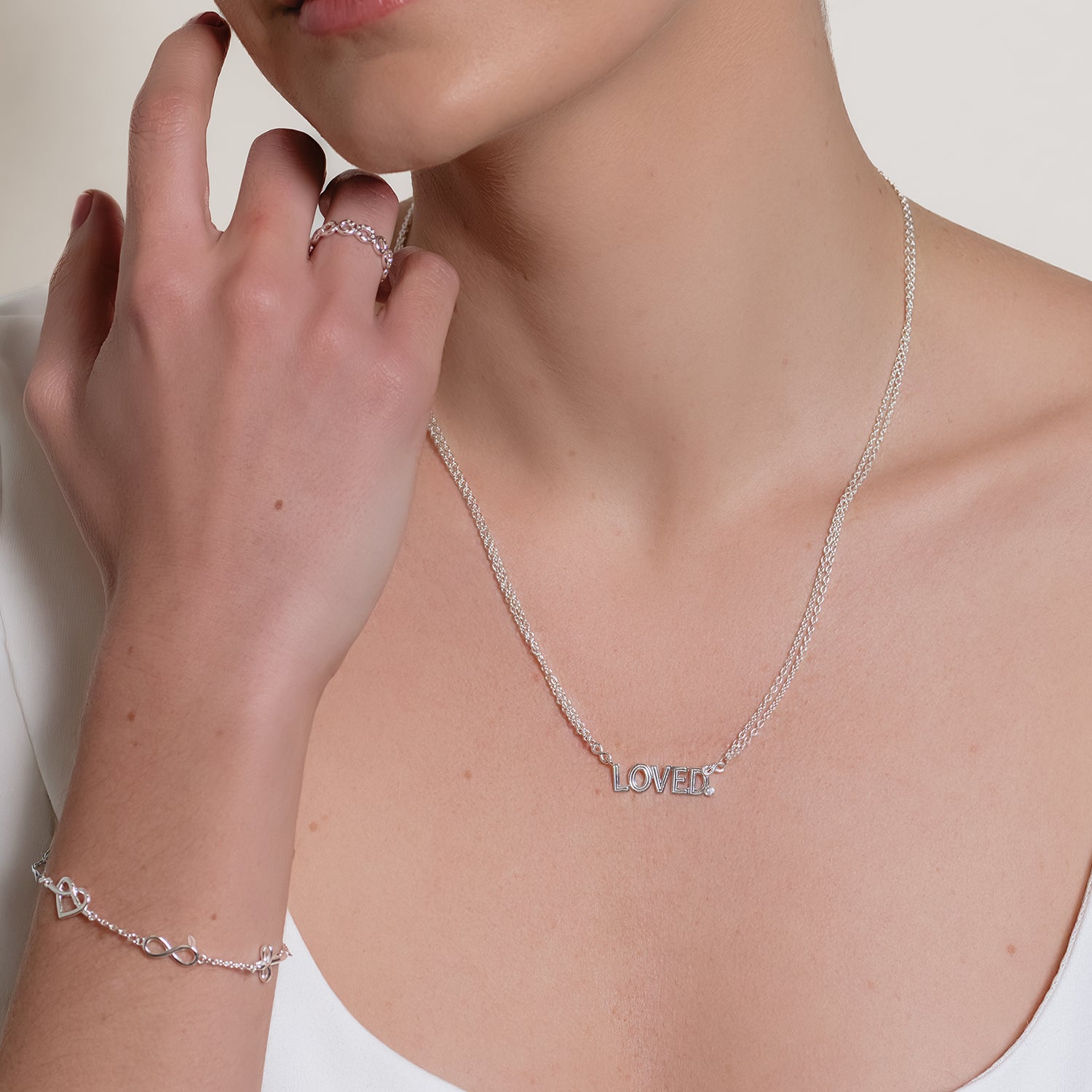 Faith Hope and Love silver bracelet worn by a female christian jewelry model with  cross, infinity, and heart charms and also wearing the Loved. necklace by Rizen Jewelry. 