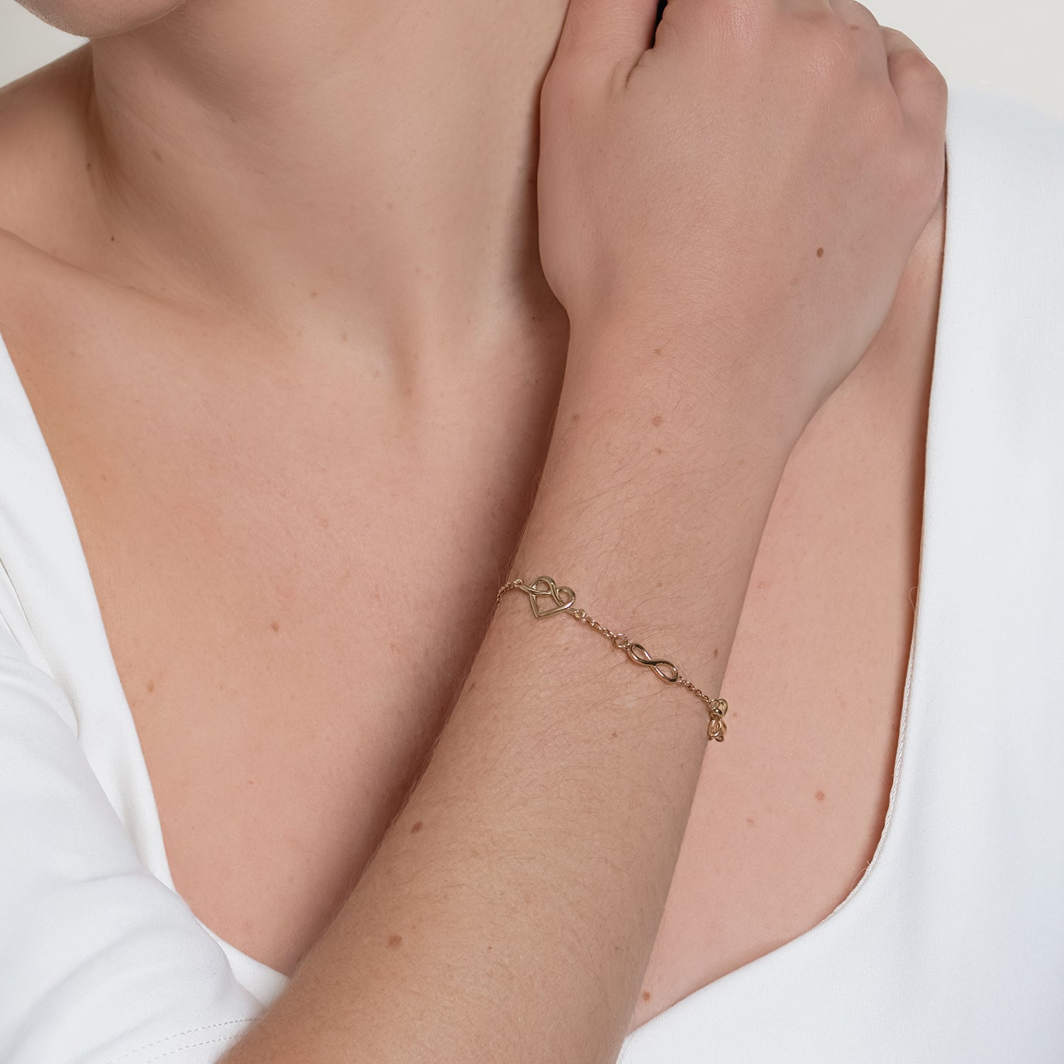 Faith Hope and Love Gold bracelet worn by a female christian jewelry model with  cross, infinity, and heart charms by Rizen Jewelry. 