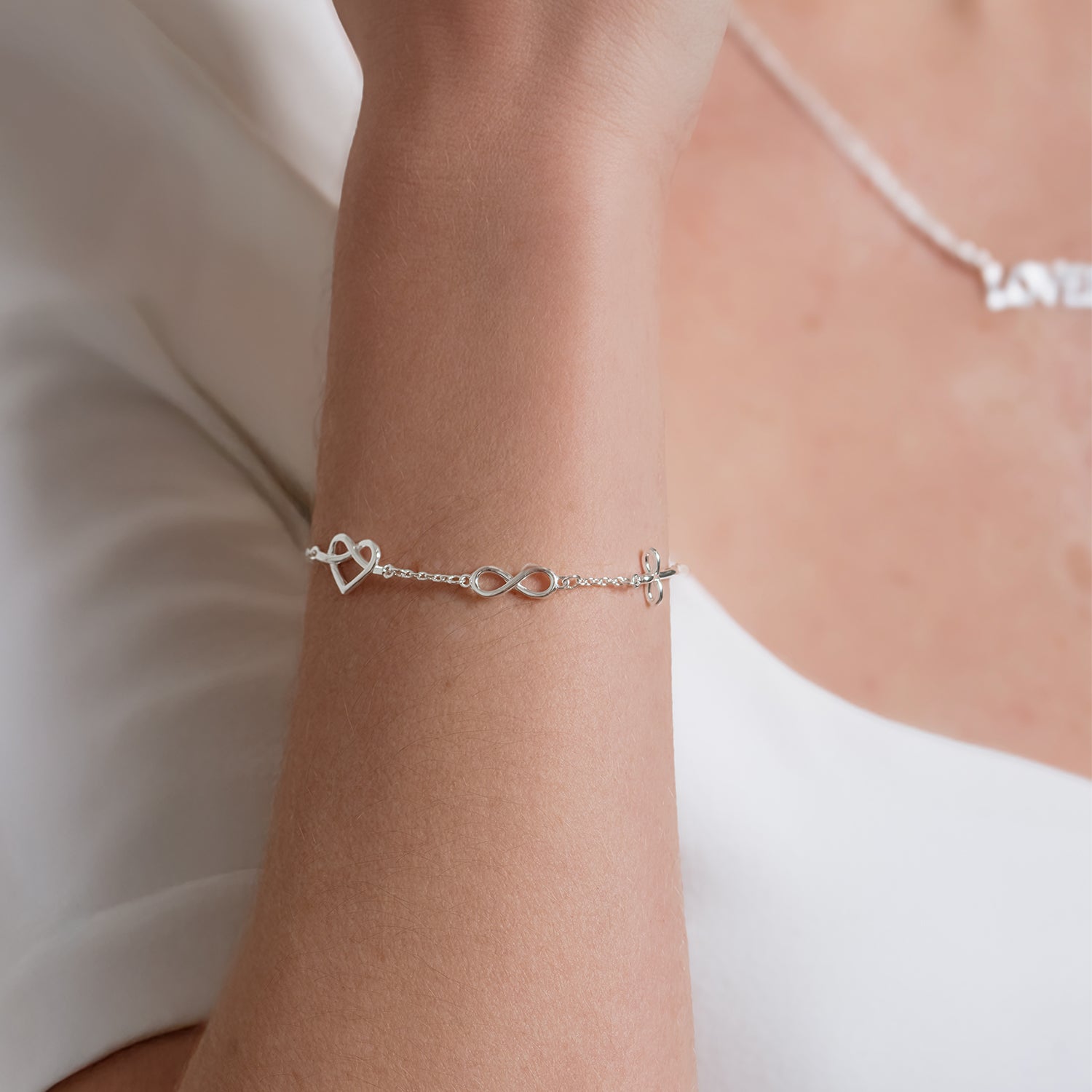 Faith Hope and Love silver bracelet worn by a female christian jewelry model with  cross, infinity, and heart charms by Rizen Jewelry. 