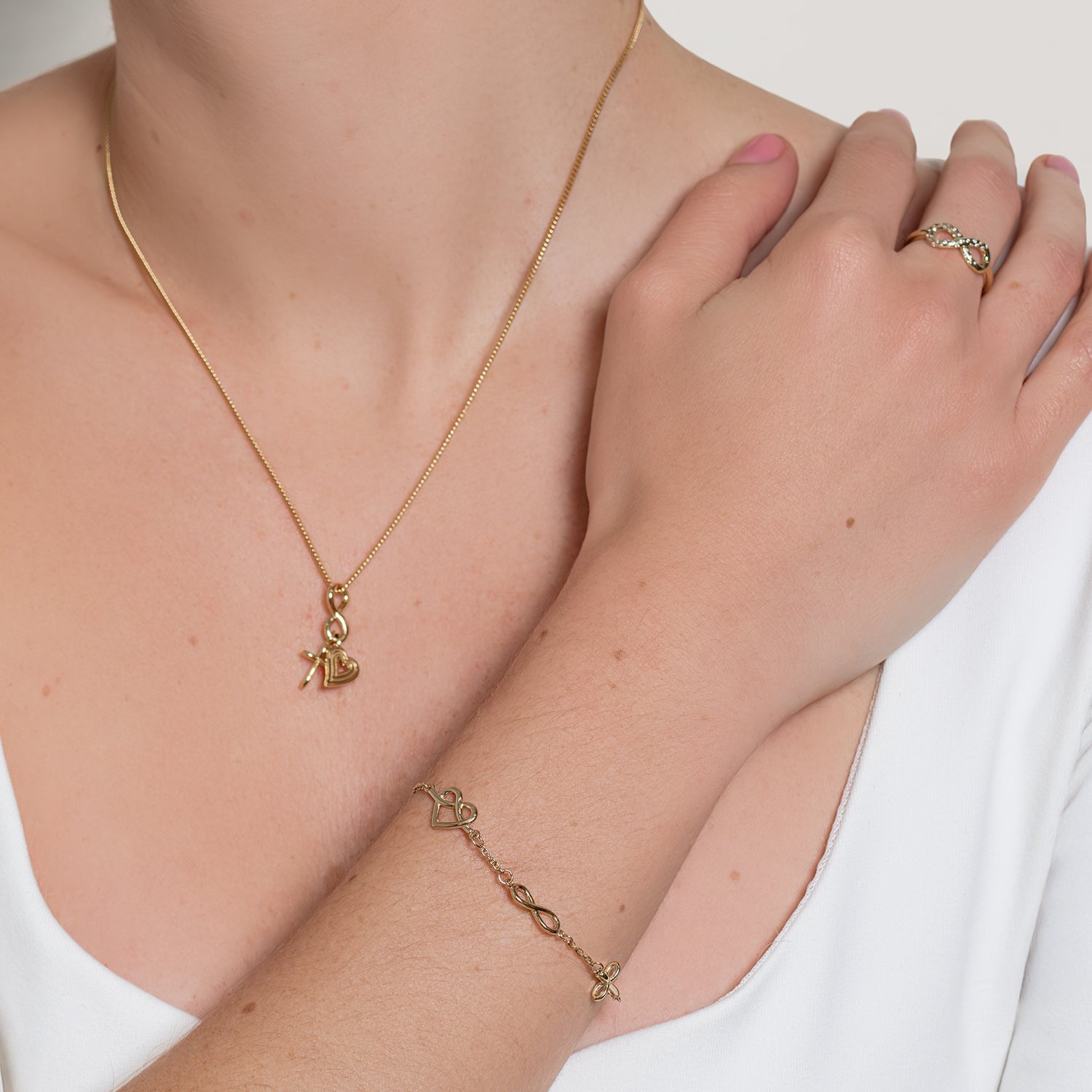 Faith Hope and Love Gold bracelet worn by a female christian jewelry model with  cross, infinity, and heart charms by Rizen Jewelry with the matching necklace. 