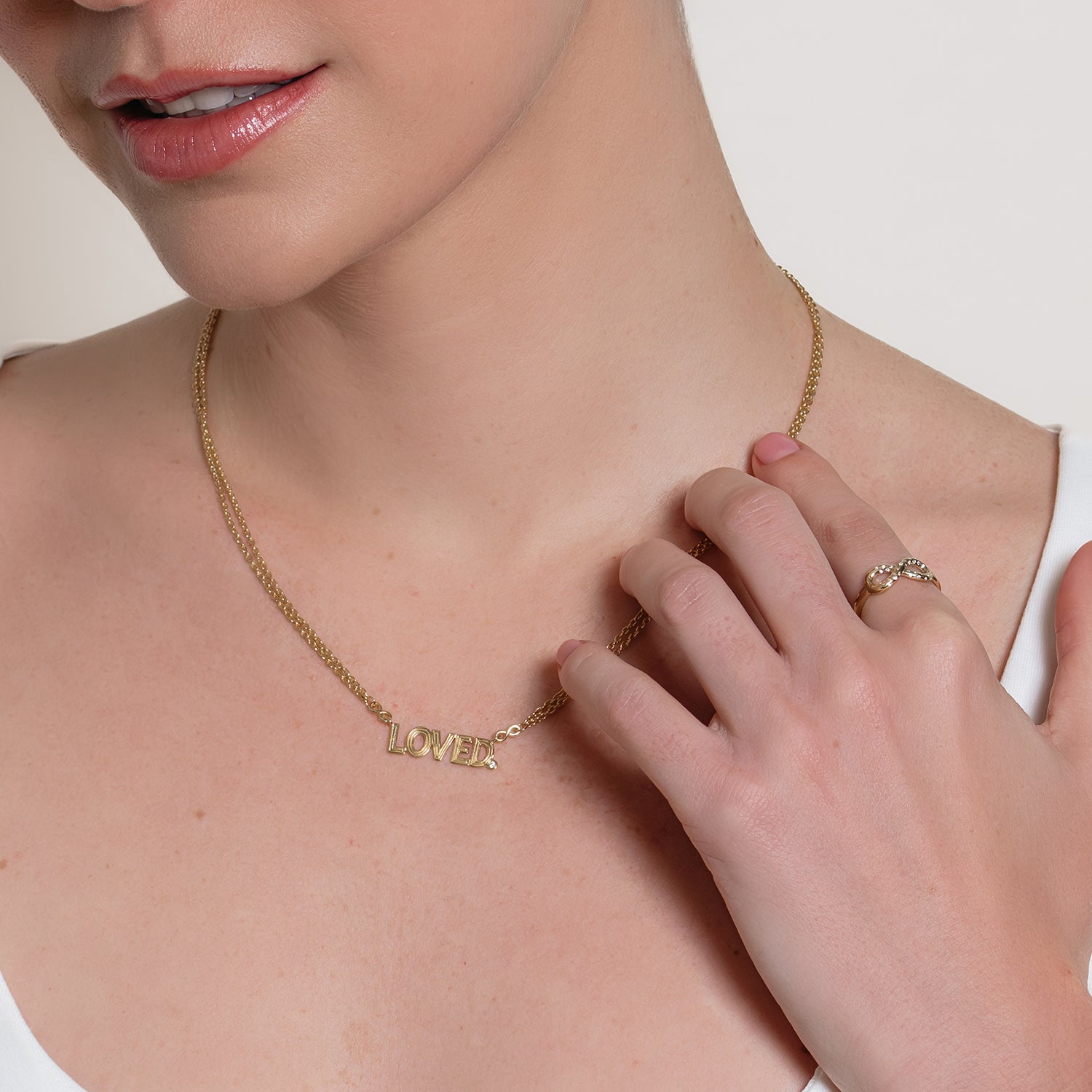 Loved. gold necklace worn by a Christian woman, with a hand touching the necklace wearing an infinity ring by Rizen Jewelry.