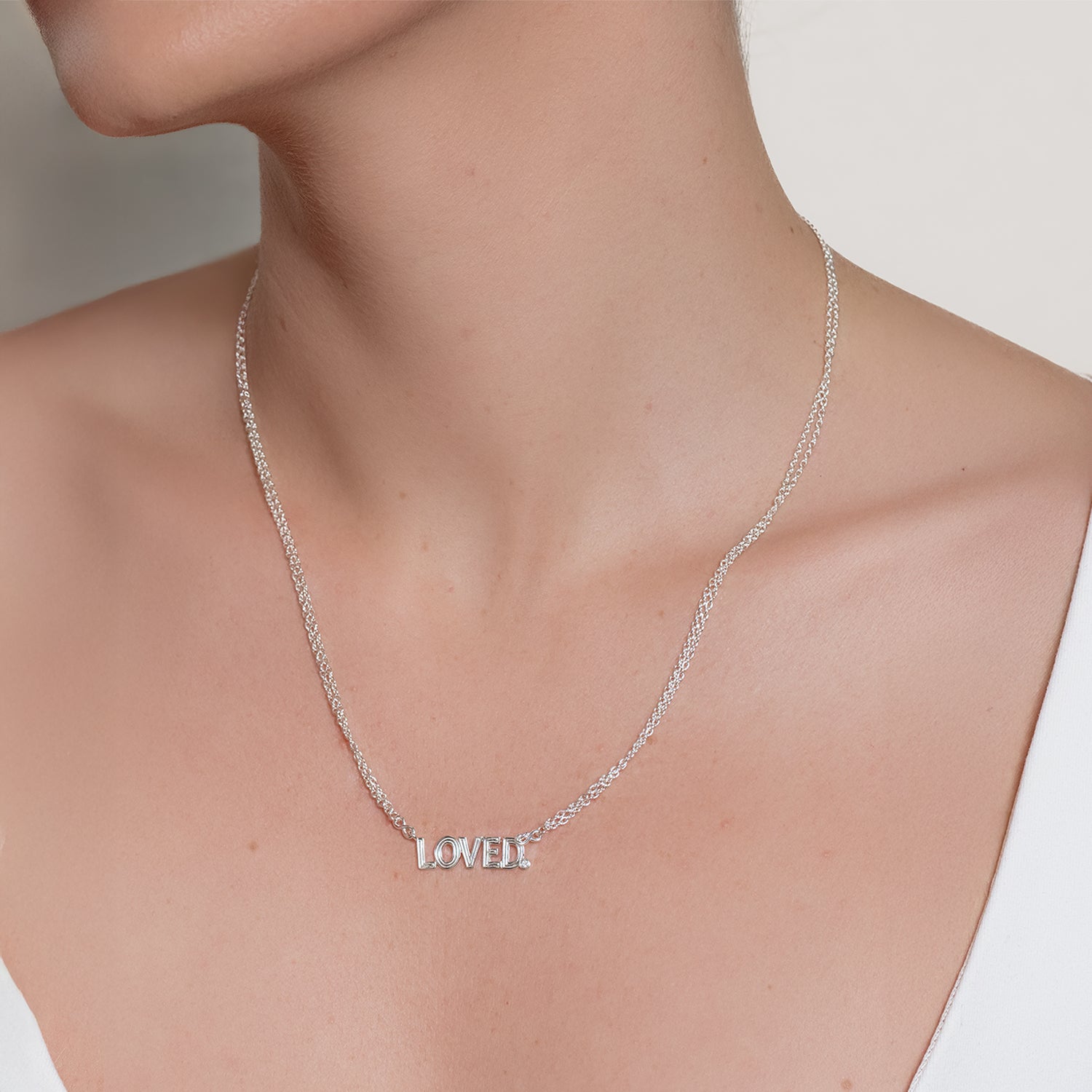Silver 'LOVED.' necklace on a Christian female model against a neutral background