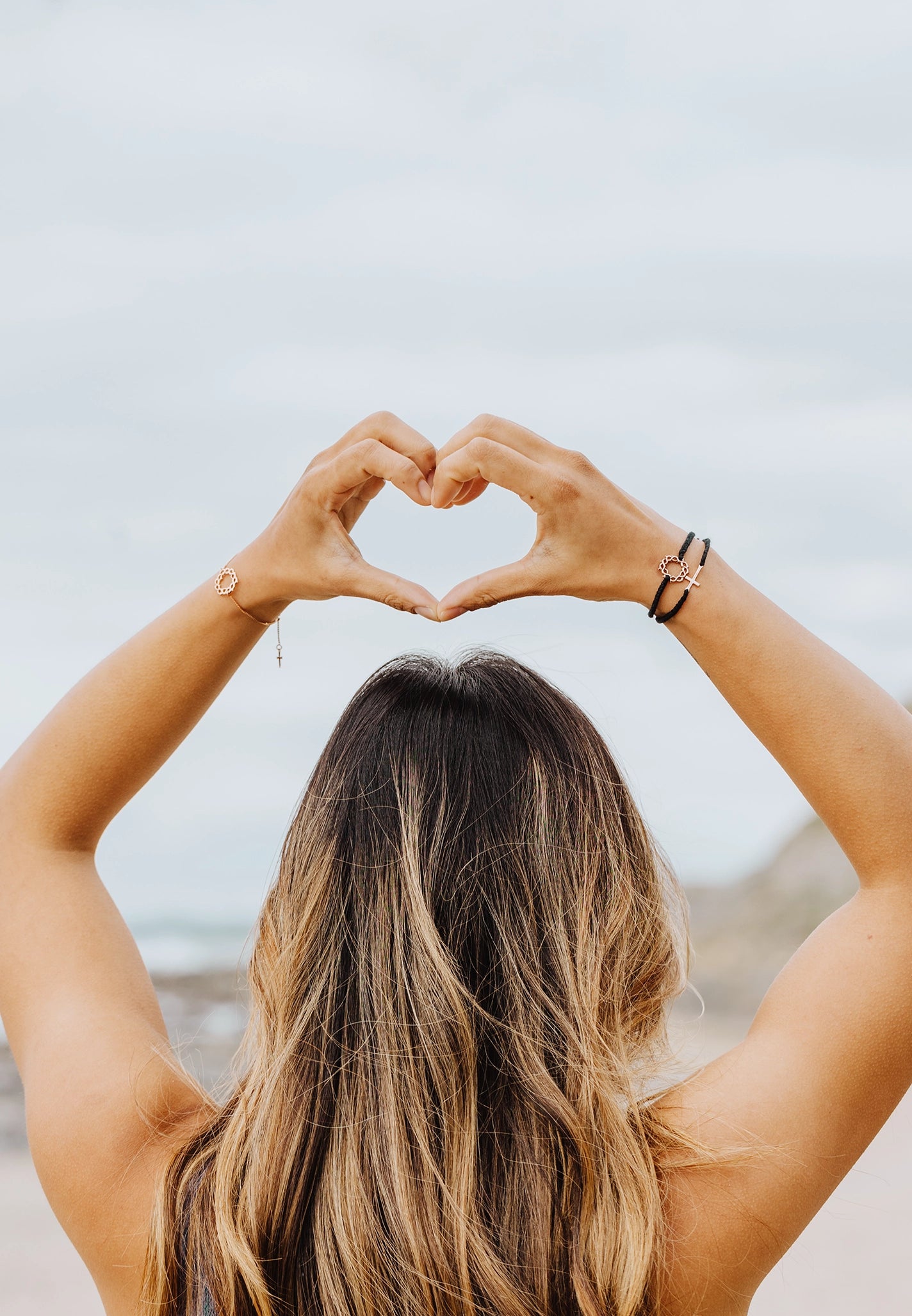 Christian young woman wearing Made4Ministry cord bracelets by Rizen Jewelry and making a heart with her hands above her head. 