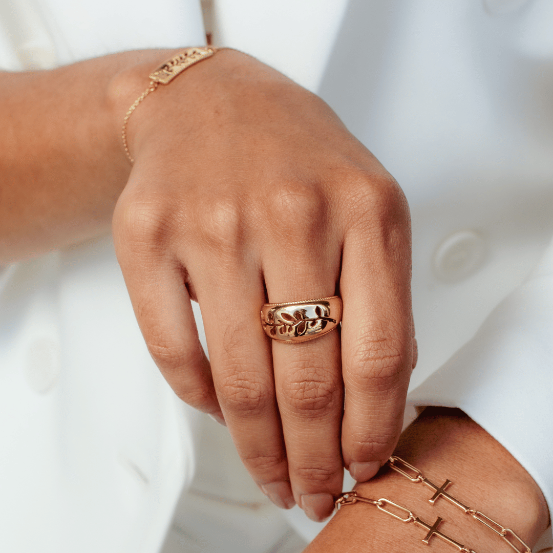 Close up of christian woman's hand wearing the 18k gold vermeil Olive branch ring and bracelet holding the chain breaker cross bracelet on opposite wrist by Rizen Jewelry. 