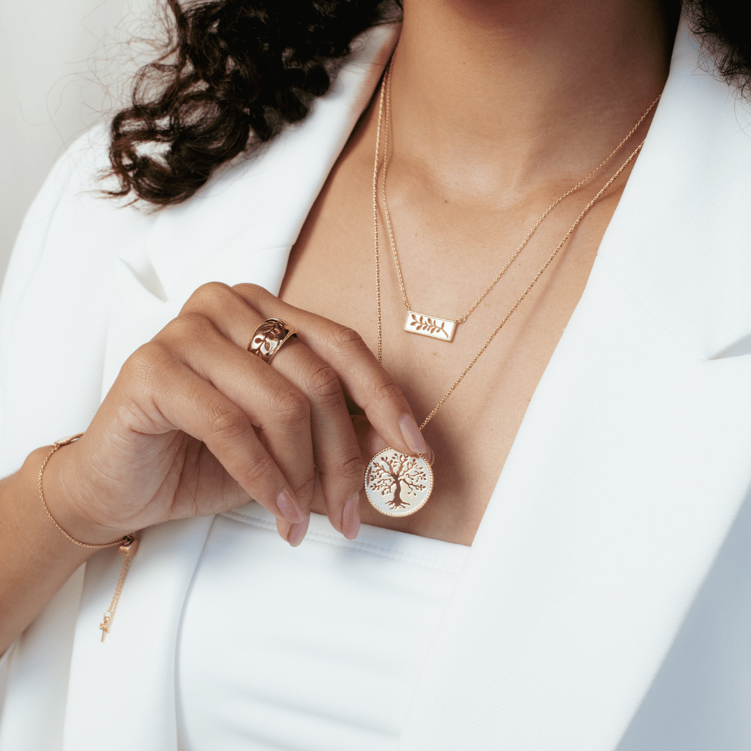 Close up of christian model wearing 18k gold vermeil Olive Tree Necklace, Olive Branch Ring, Bracelet, and Necklace from the Rooted Collection by Rizen Jewelry. 