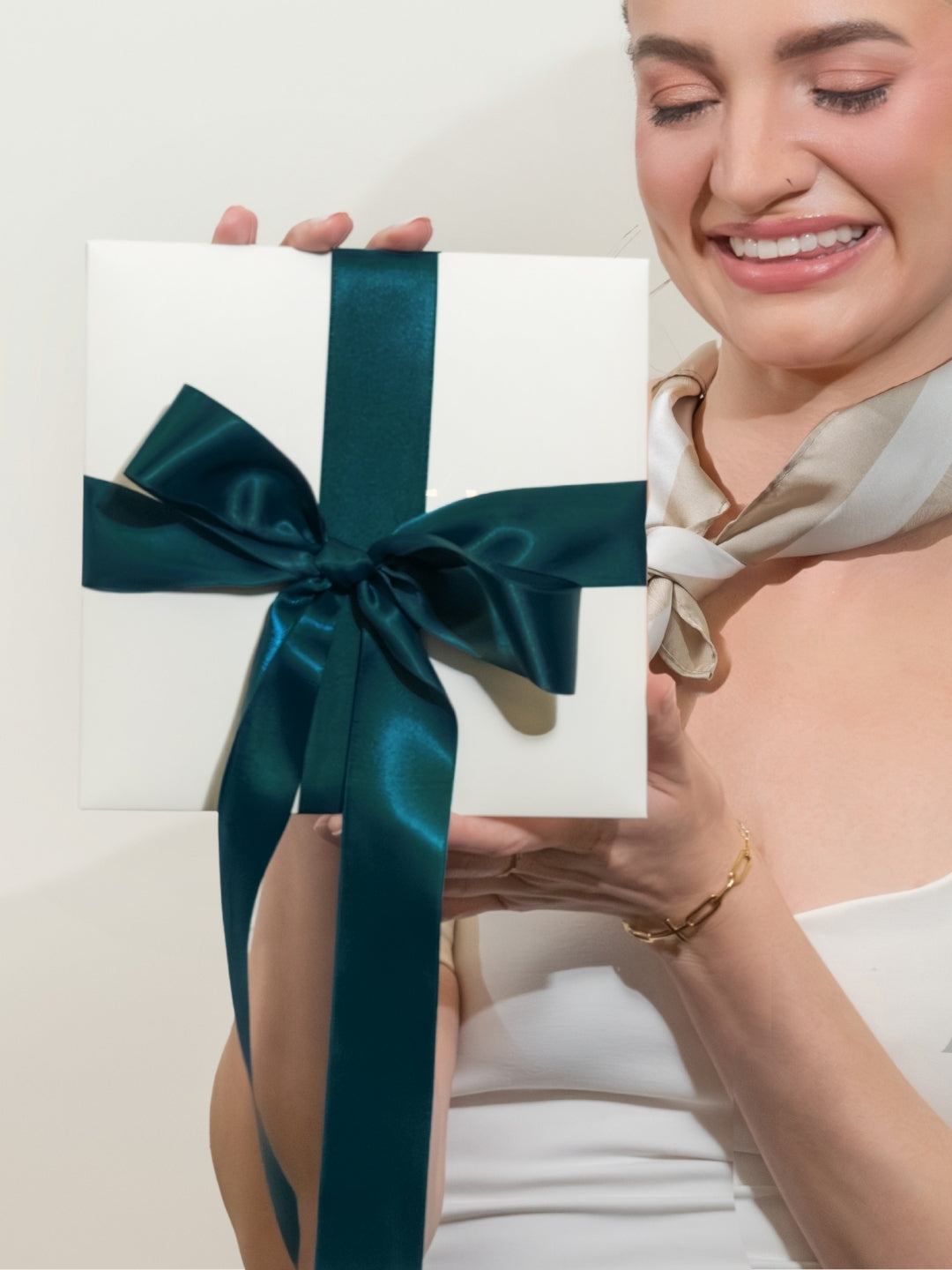 Christian Woman wearing the Rizen Scarf holding a white gift box packaging with a blue ribbon against a plain background