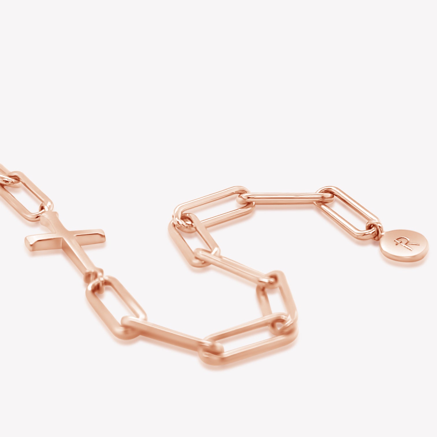 Rizen Jewelry Chain Breaker bracelet in 18k rose gold plated.  Elegant Cross Pendant breaks up the contemporary paper clip link chain with circular Rizen tag on last link of chain.