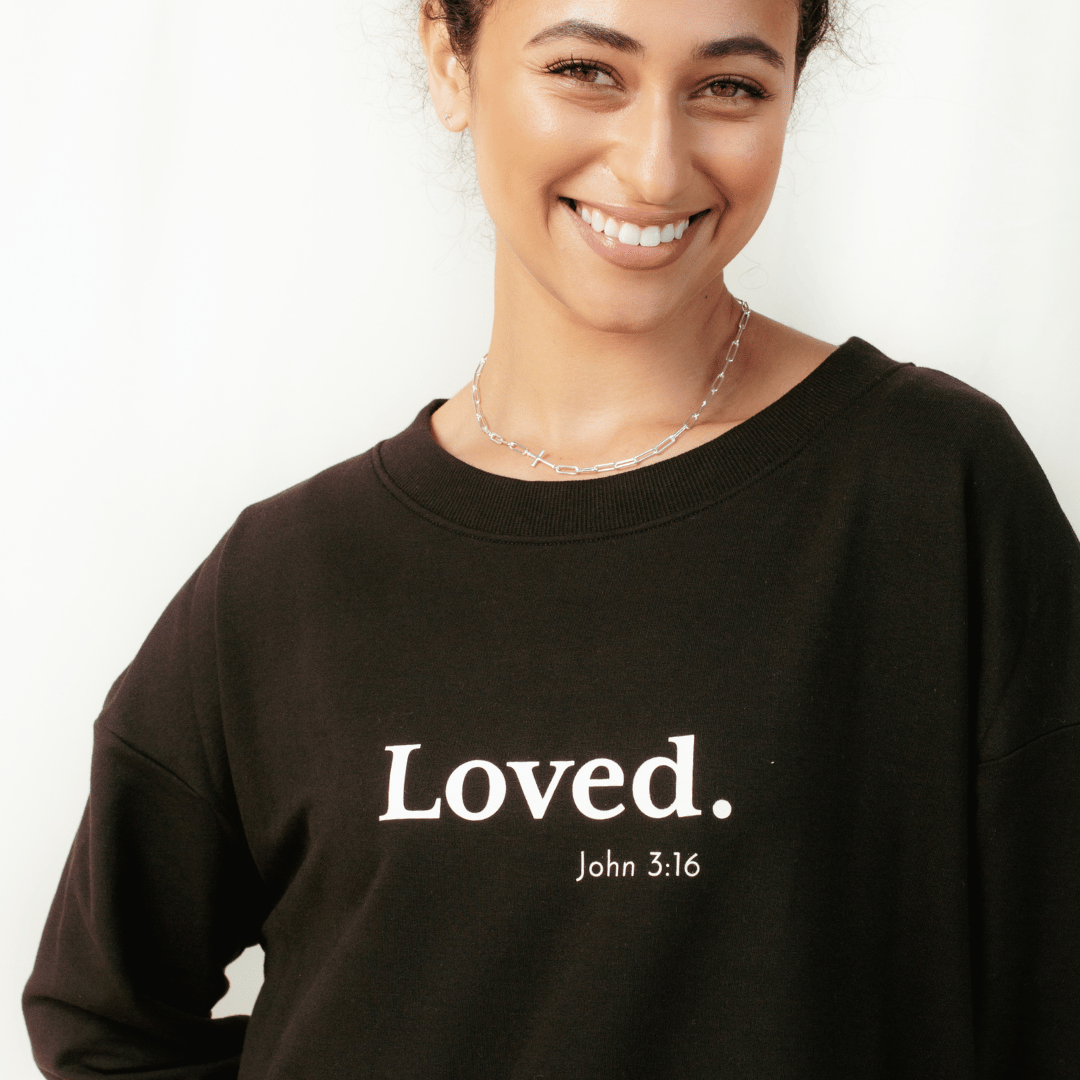 Close up of christian woman wearing the black " Loved. John 3:16" Peruvian cotton sweatshirt from the Be The Light Collection by Rizen Jewelry.