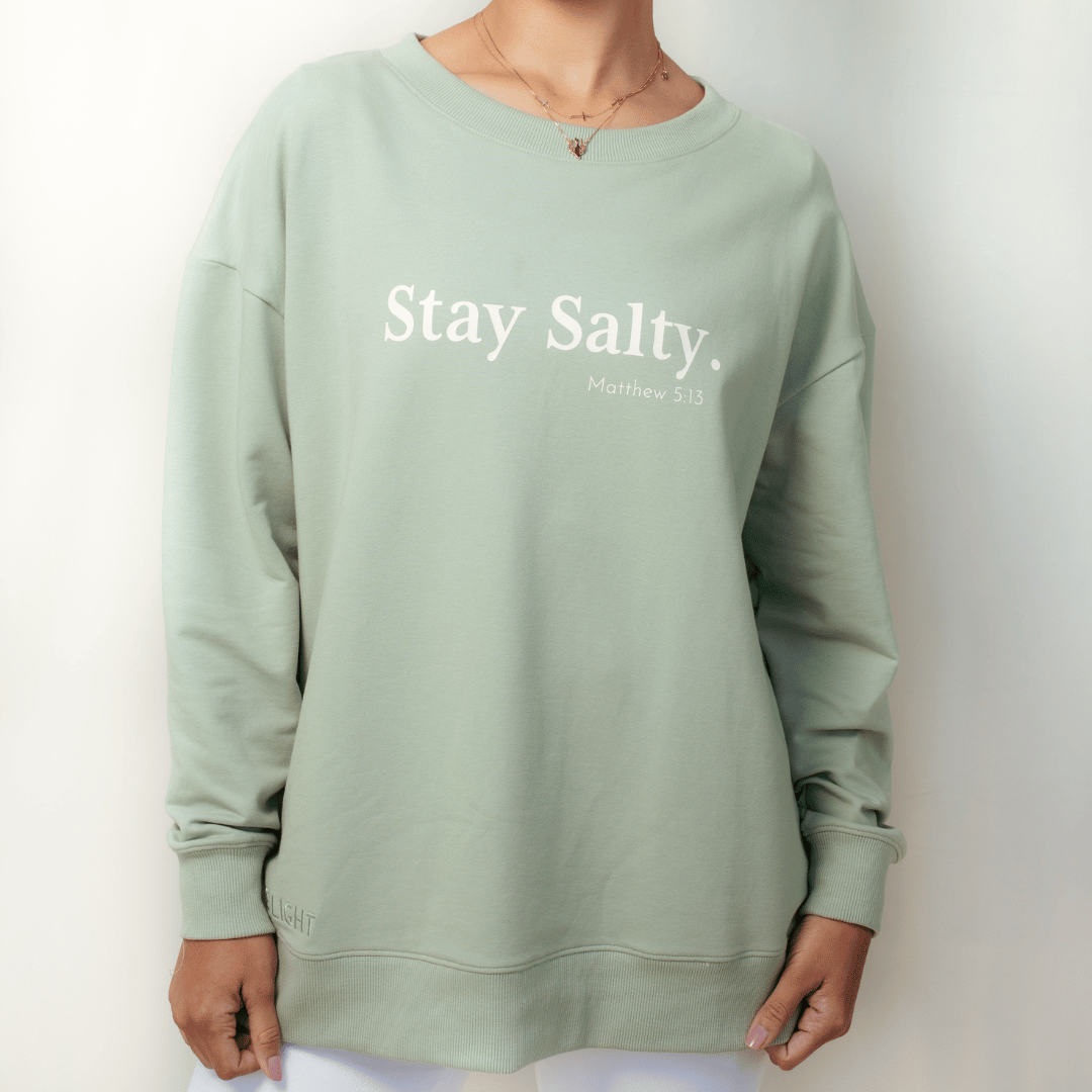Christian woman wearing the wave green "Stay Salty. Matthew 5:13" Peruvian cotton crew sweatshirt from the Be The Light Collection by Rizen Jewelry.