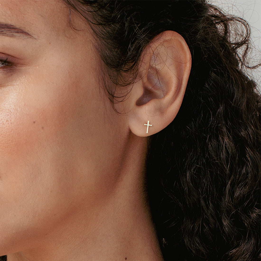 Close up of Christian woman wearing mini Cross stud Earrings in 18k gold vermeil from the Calvary Collection by Rizen Jewelry.