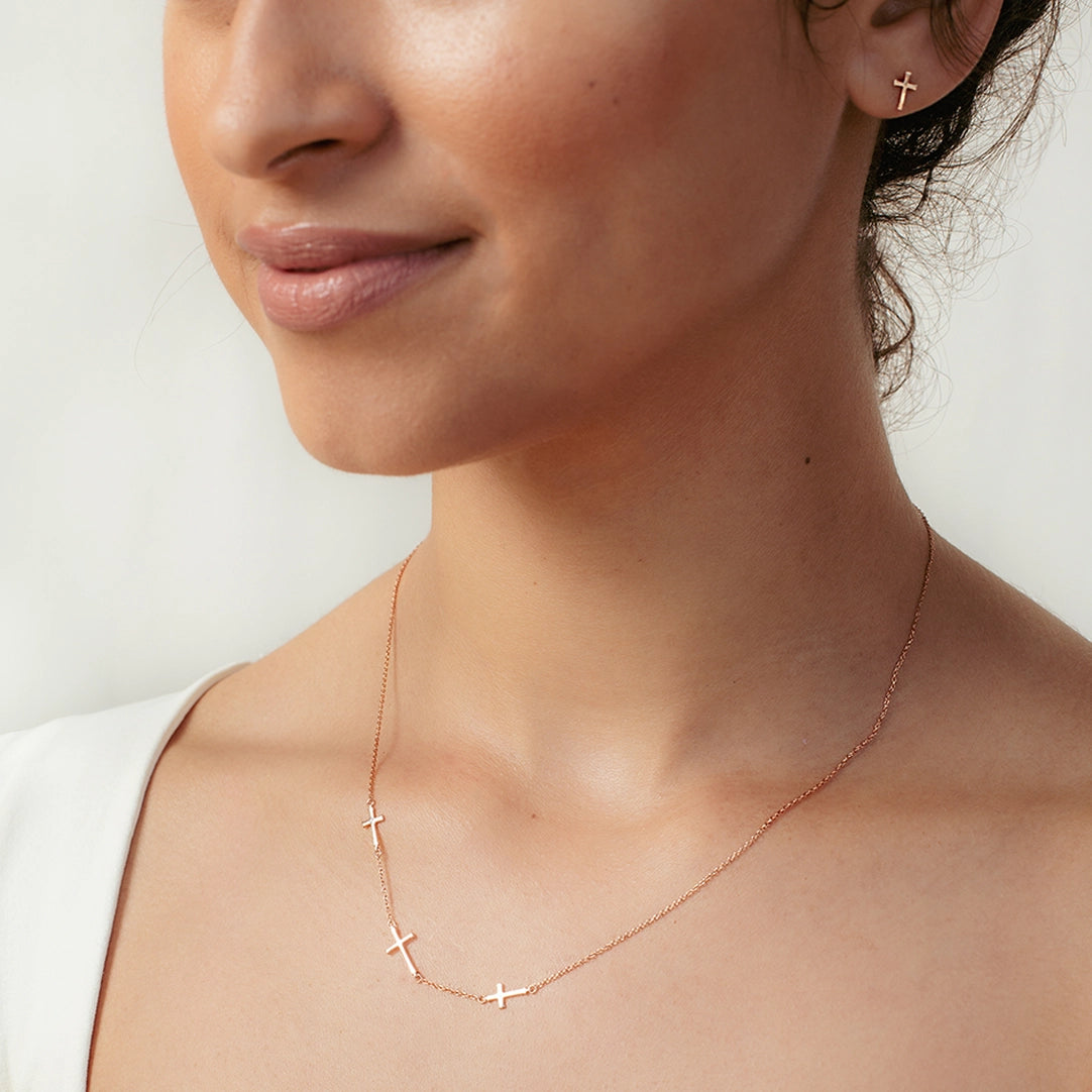 Christian woman wearing rose gold triple cross Calvary Necklace and Mini Cross Stud Earrings from the Calvary Collection by Rizen Jewelry.