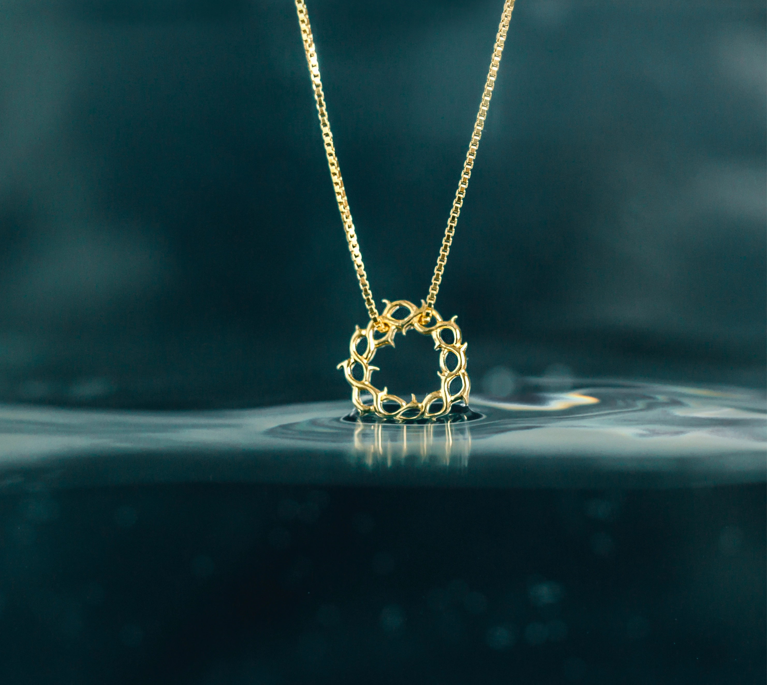 The gold vermeil Crown of Thorns Necklace from the Insignia Collection by Rizen Jewelry dipping in water with depth color background.