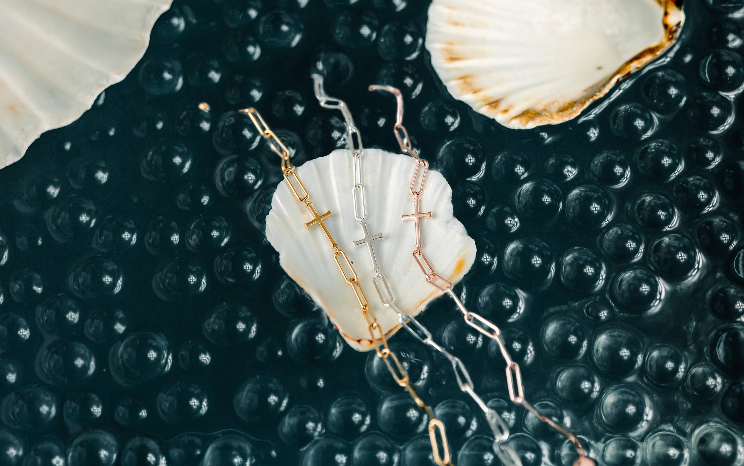 gold vermeil, sterling silver, and rose gold vermeil cross and paper clip chain bracelets in a scallop sea shell