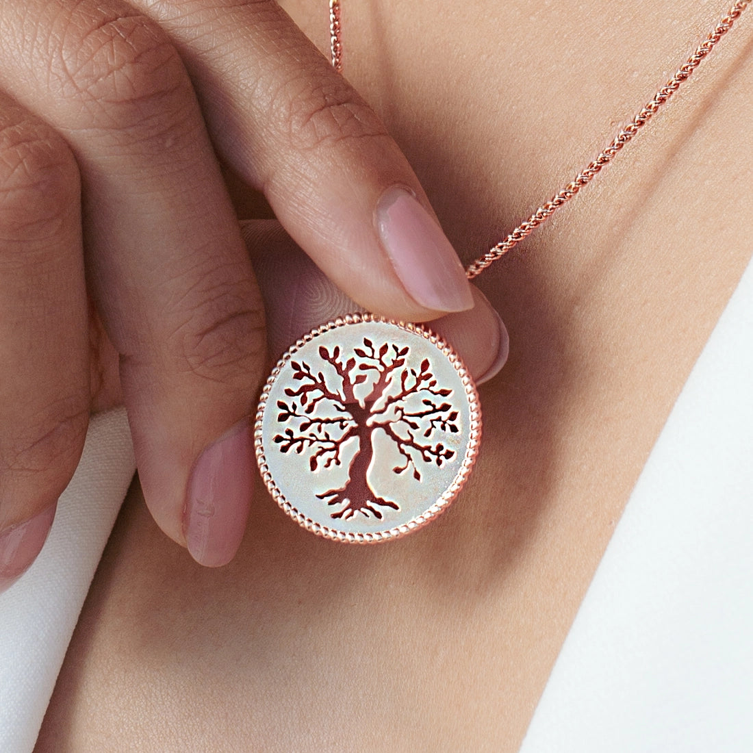 Close up of christian woman holding and wearing the Olive Tree Necklace in 18k rose gold vermeil from the Rooted Collection by Rizen Jewelry.