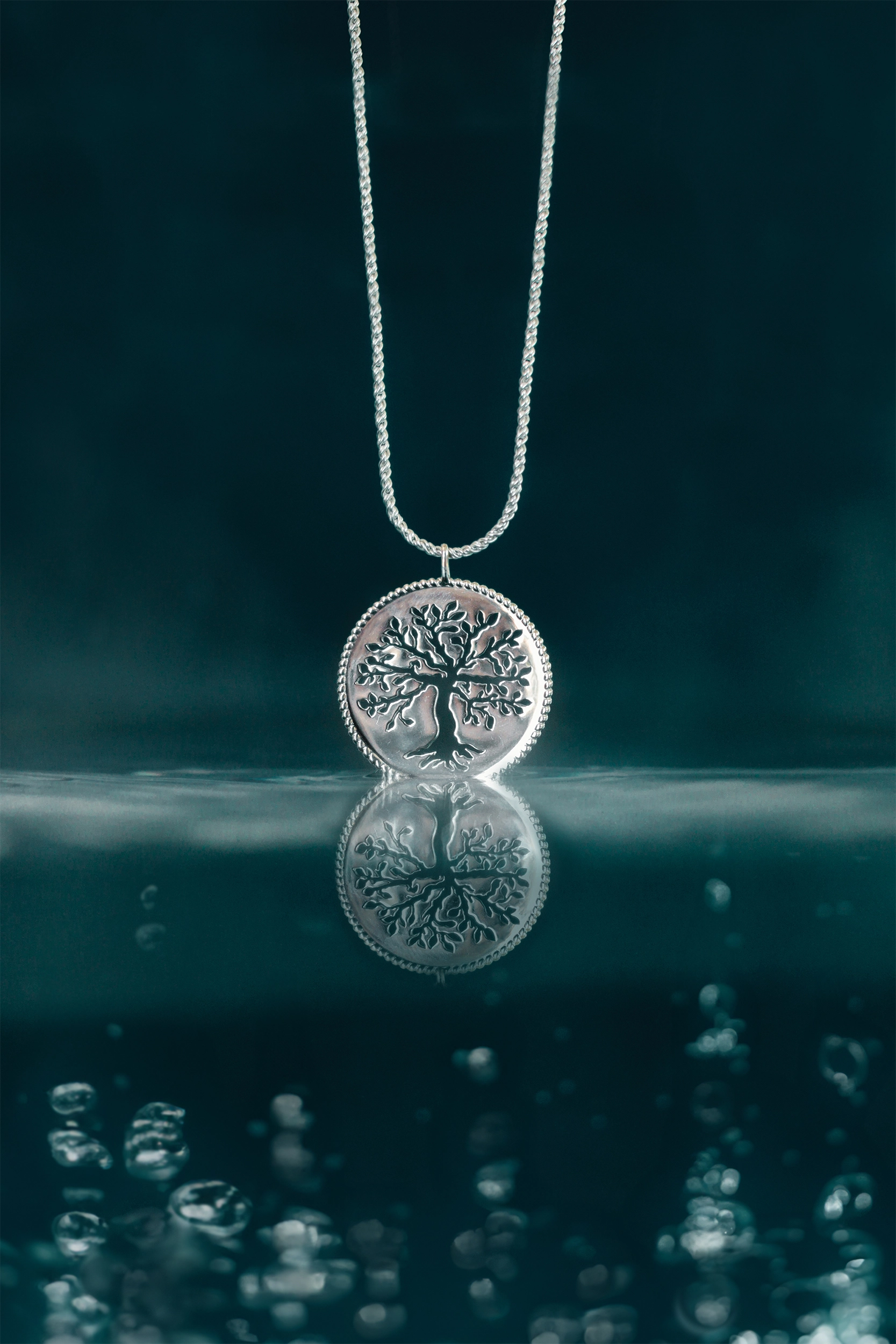 Rizen Jewelry Rooted Olive Tree necklace in sterling silver dipping into depth colored water. 