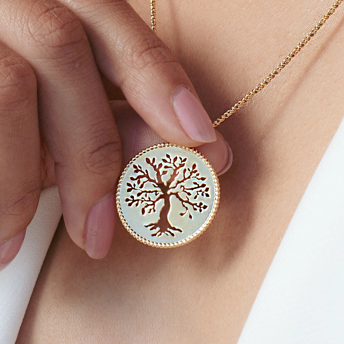 Close up of christian woman holding and wearing the 18k gold vermeil Olive Tree Necklace from the Rooted Collection by Rizen Jewelry.