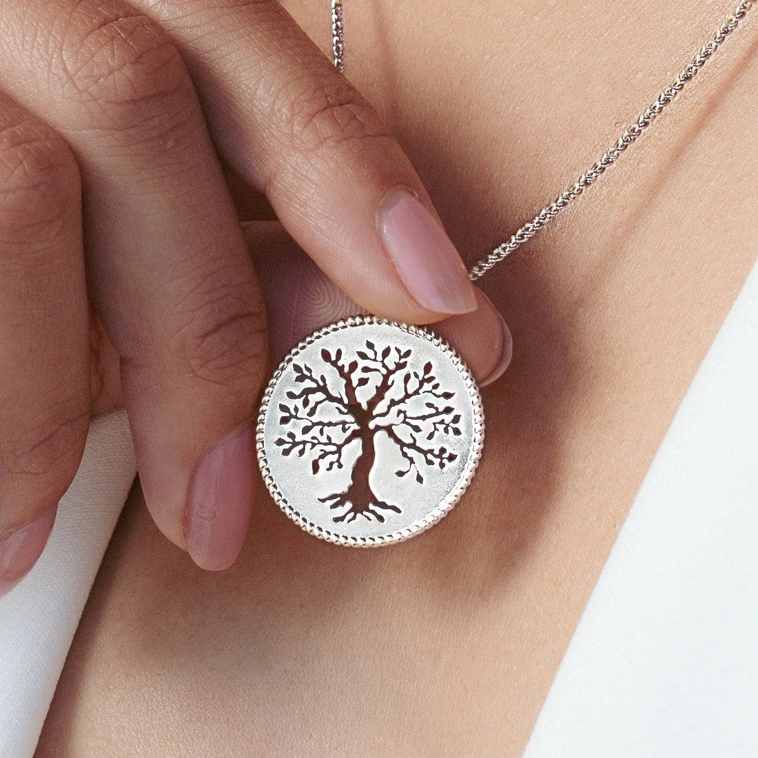 Close up of christian woman holding and wearing the sterling silver Olive Tree Necklace from the Rooted Collection by Rizen Jewelry.