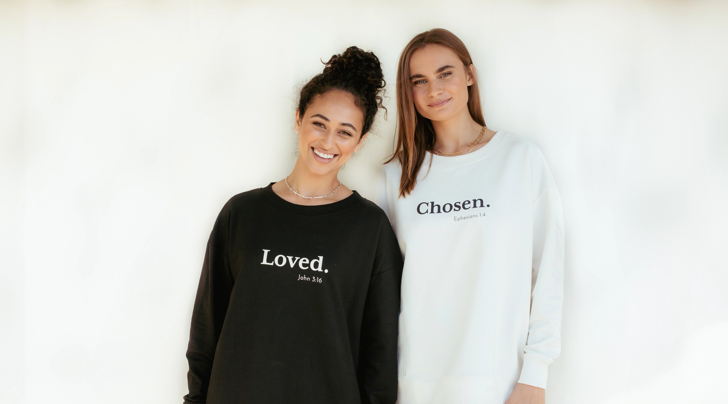 Two Christian ladies wearing Be The Light sweatshirts from Rizen Jewelry with positive messages of "Loved. John 3:16" and "Chosen. Ephesians 1:4".