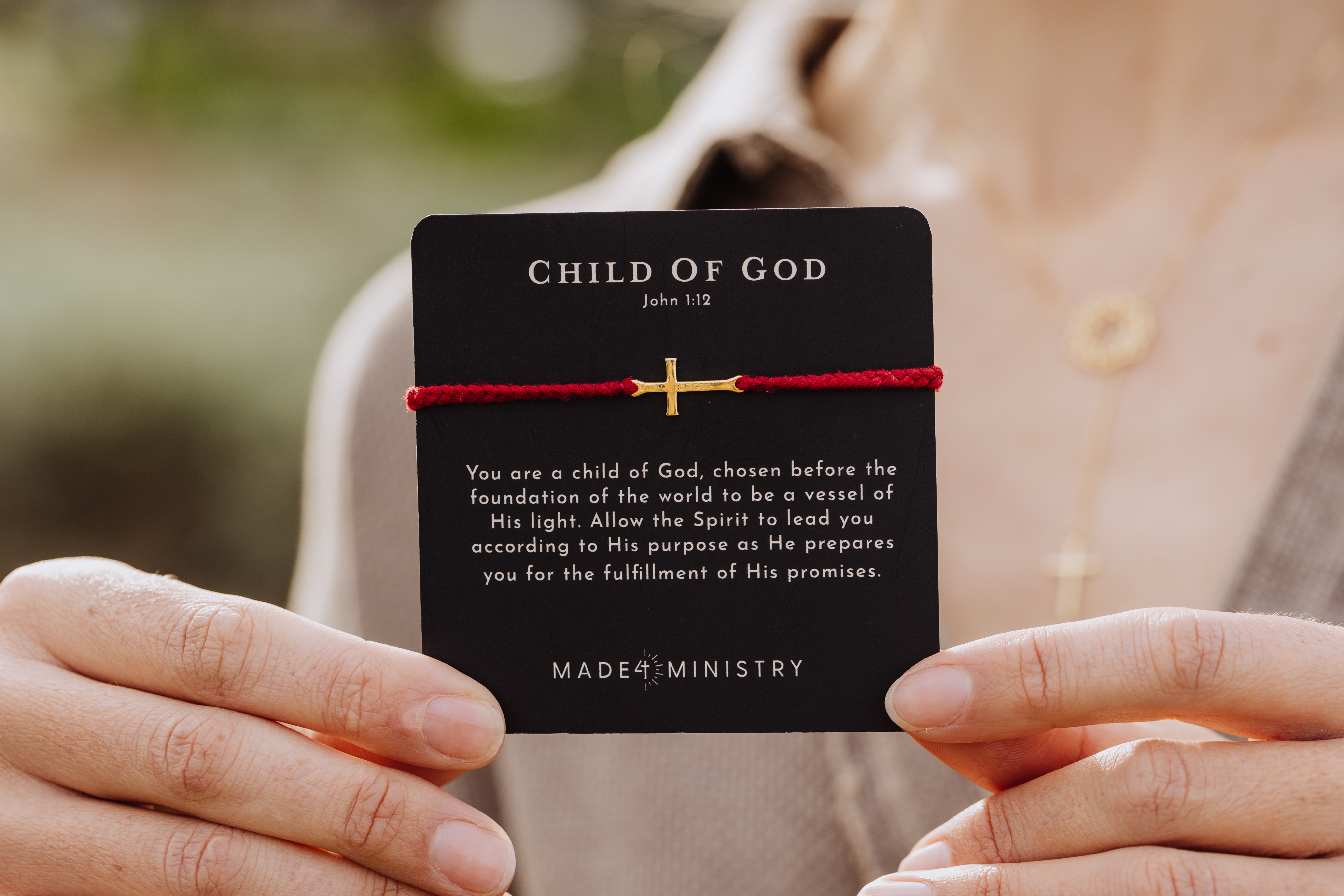 Christian model holding Made 4 Ministries Child of God garnet red gold cross braided friendship bracelet on devotion card by Rizen Jewelry