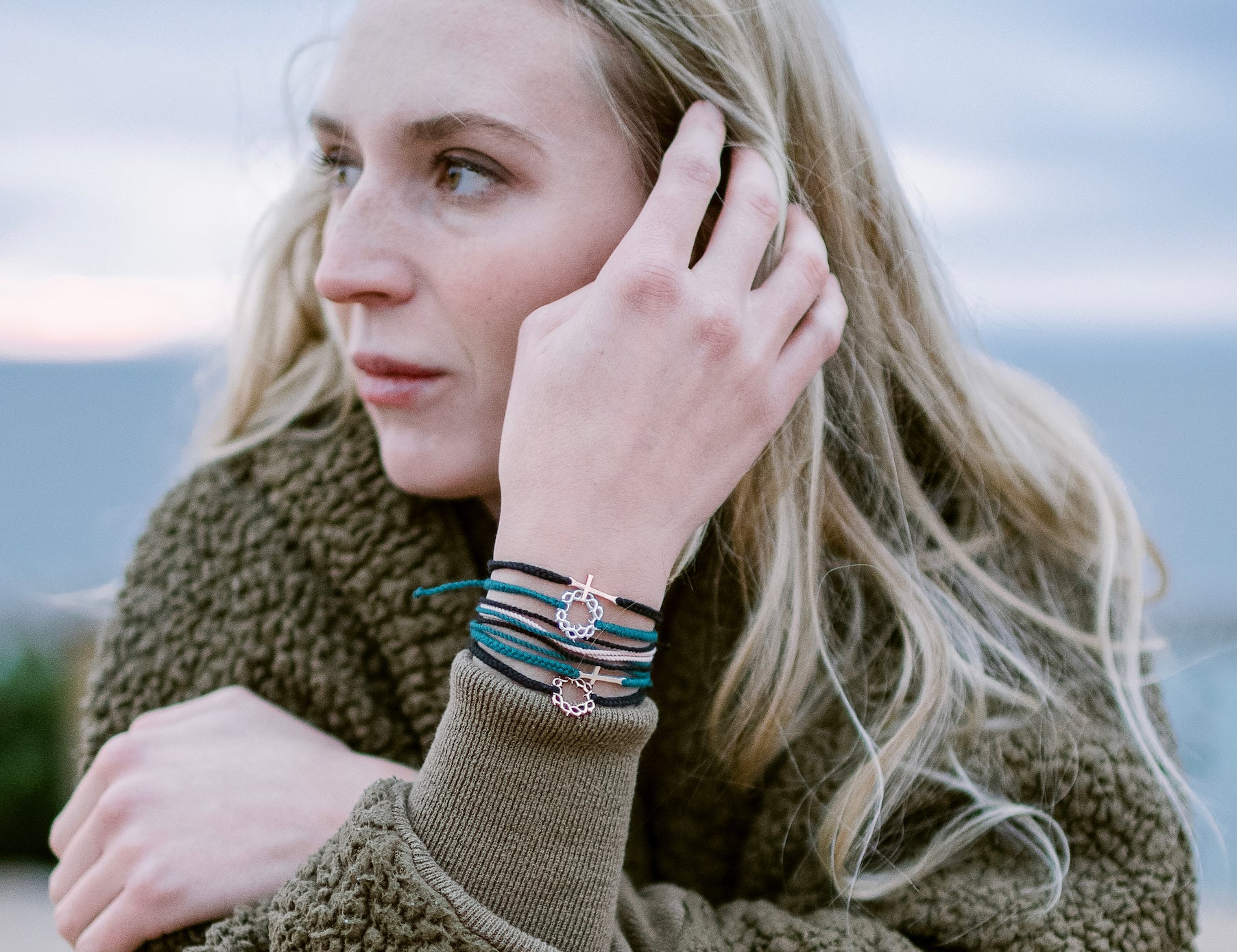 Model wearing christian friendship bracelet with silver crown of thorns pendant on hand braided azure blue cotton cords by Rizen Jewelry. Layered with multiple Made 4 Ministries collection bracelets.