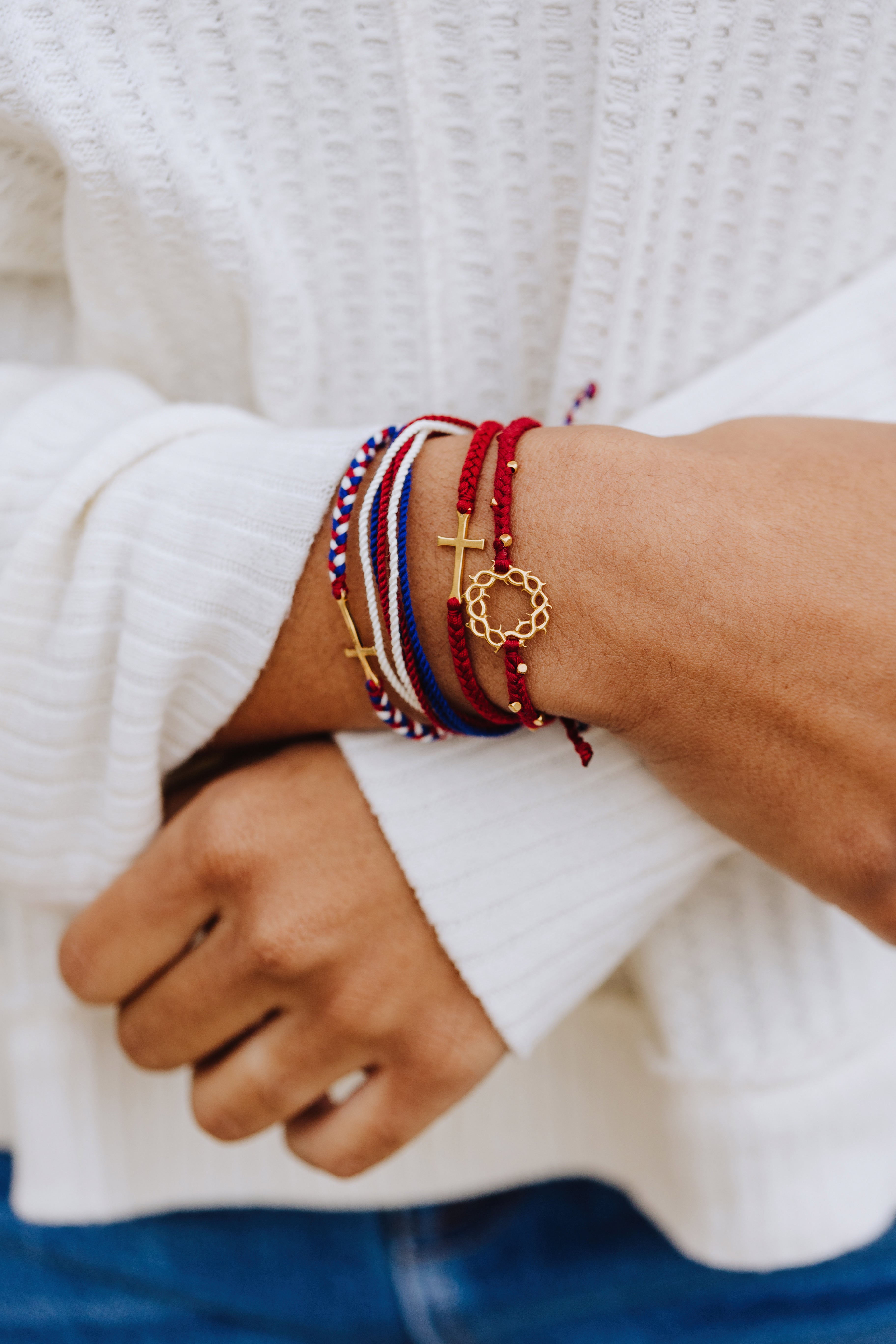 Christian Model wearing red white and blue be magnified peaceful bracelet layered with the gold we trust in god cross bracelet, and garnet red crown of thorns and stay salty cross friendship bracelets by Rizen Jewelry Made 4 Ministries collection.